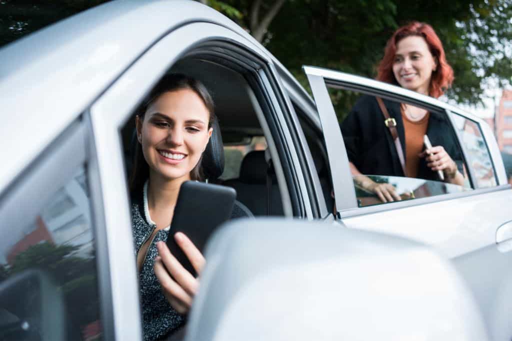 A woman holding up her phone as she is getting out of a silver car