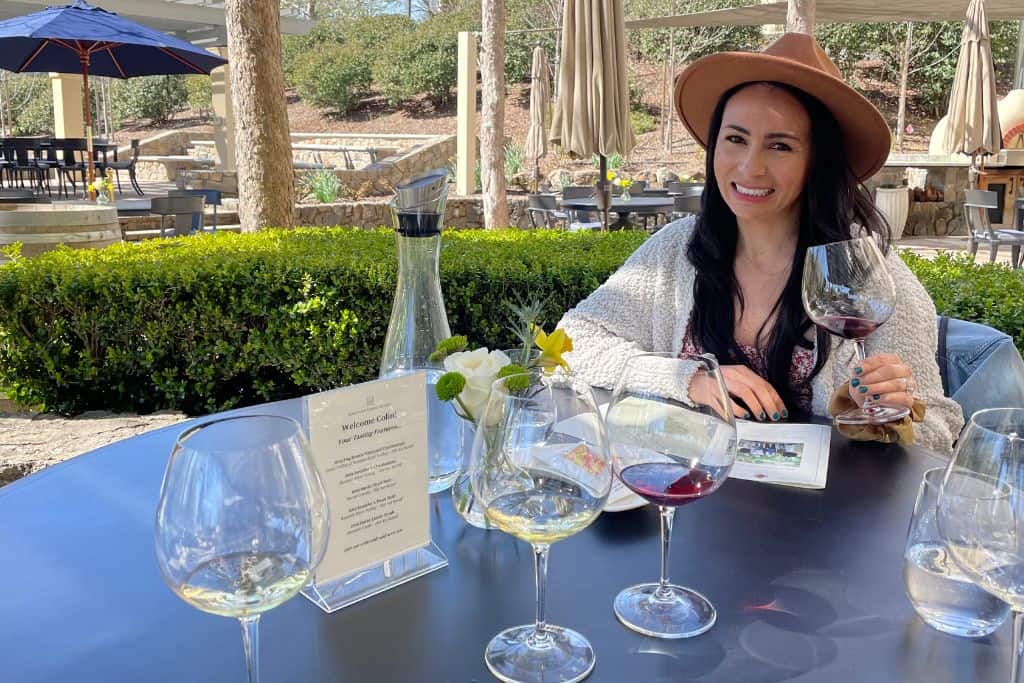 Woman with a wide brimmed hat sitting with a wine tasting and a glass of red wine in her hand