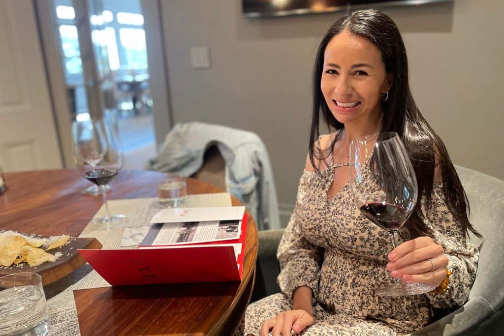A woman with long dark hair enjoying a wine tasting with a glass of red wine in her hand