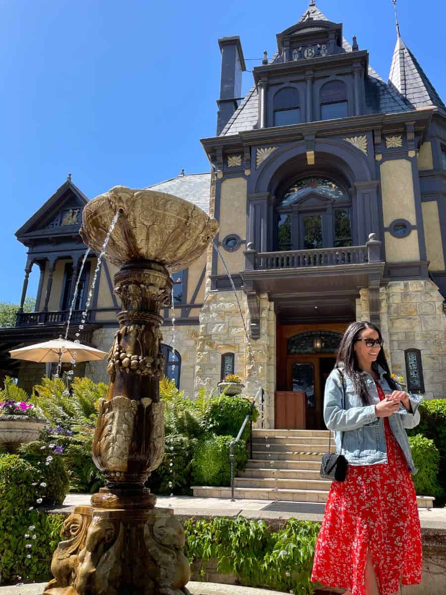 A woman with a jean jacket and dress standing in front of a historic building and fountain