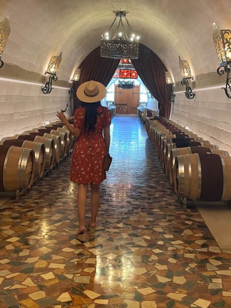 A woman in a dress with a wide brimmed hat touring the beautiful marble wine caves and wine barrels at Piazza Del Dotto